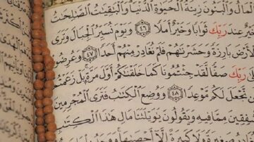 نص من القرآن الكريم يظهر في صفحة مكتوبة بخط عربي جميل، مع وجود مسبحة خشبية على الجانب. النص يتضمن آيات تتعلق بالتوجيه والإيمان.