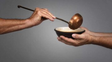 يد تحمل مغرفة نحاسية تصب في وعاء أسود، بينما تُمد يد أخرى لتلقي الطعام. تعكس الصورة مفهوم المشاركة والكرم.