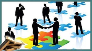 رجلان يرتديان بدلات رسمية يتصافحان على قطعة من أحجية ملونة، بينما تظهر شخصيات أخرى في الخلفية على قطع أحجية زرقاء. في الزاوية، توجد مجموعة من الكتب. تعكس الصورة مفهوم التعاون والشراكة في بيئة العمل.