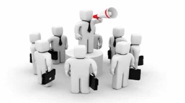 شخصية ثلاثية الأبعاد ترتدي بدلة وتستخدم ميكروفونًا، واقفًا على قاعدة، محاطة بعدد من الشخصيات الأخرى التي تحمل حقائب. تعكس الصورة مفهوم القيادة والتوجيه في بيئة العمل.