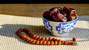 طبق مزخرف يحتوي على تمر من النوع الجاف، موضوع على قماش محايد، بجانب مسبحة خشبية تقليدية.