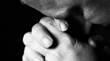 رجل يضع رأسه على يديه المضمومتين في التعبير عن التأمل أو الحزن، مع خلفية داكنة تعزز من عمق الصورة.