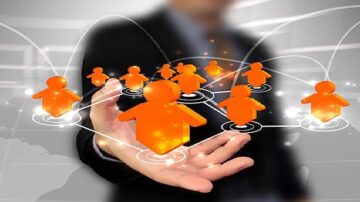 رجل يرتدي بدلة يحمل بيده رموزاً برتقالية تمثل الأشخاص، مع خطوط متصلة تشير إلى الشبكات والتواصل. الخلفية توضح رسمًا بيانيًا مع تفاصيل خفيفة لعالم متصل. الصورة تعبر عن مفهوم الشبكات الاجتماعية والتواصل الرقمي.