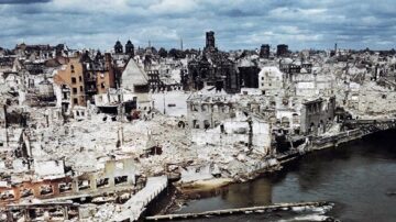 صورة توضح دمار مدينة تاريخية بعد تعرضها للغارات الجوية، مع مباني مهدمة وأطلال تنتشر في المشهد. يظهر نهر يمر عبر المنطقة المدمرة تحت سماء غائمة، مما يعكس آثار الحرب والدمار.