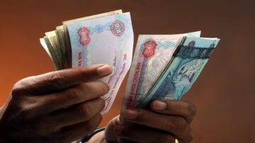 رجل يحمل أوراق نقدية من فئات مختلفة، بما في ذلك عملة إماراتية، مع خلفية داكنة. تعكس الصورة التعاملات المالية والاقتصاد.