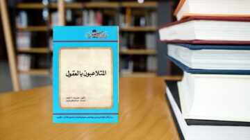كتاب "المتعلمون بالمعتقل" يظهر على طاولة خشبية، محاطًا بمجموعة من الكتب الأخرى. الخلفية تحتوي على رفوف كتب في مكتبة. الكتاب ذو غلاف أزرق، مع نص عربي واضح في المنتصف.