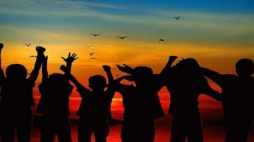 أطفال silhouettes يرفعون أيديهم في الهواء عند غروب الشمس، مع سماء ملونة بالبرتقالي والأزرق. طيور تحلق في الخلفية، تعبير عن الفرح والحرية.