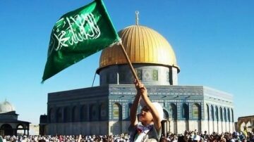 طفل يحمل علم السعودية أمام قبة الصخرة في المسجد الأقصى، مع حشد كبير من الناس في الخلفية، تحت سماء زرقاء صافية.