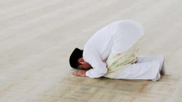 رجل مسلم يؤدي صلاة السجود على أرضية المسجد، يرتدي ملابس تقليدية ويظهر في وضع احترام وخشوع.