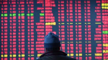 شخص يرتدي قبعة زرقاء ينظر إلى شاشة عرض للأسواق المالية مغطاة بأرقام حمراء وخضراء، تعكس تقلبات الأسهم.