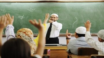 مدرس يتحدث أمام طلاب في فصل دراسي، يرفع الطلاب أيديهم للإجابة، خلفية سوداء مع رسمات بيضاء.