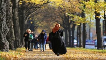 امرأة ترتدي الحجاب تسير على ممر محاط بأشجار بأوراق صفراء، بينما يتجول آخرون في أجواء خريفية.