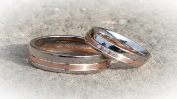 خواتم زفاف فضية وذهبية مع تفاصيل ماسية، موضوعة على سطح خشن. تعكس الخواتم الحب والالتزام، وتبرز تصميمها الأنيق.