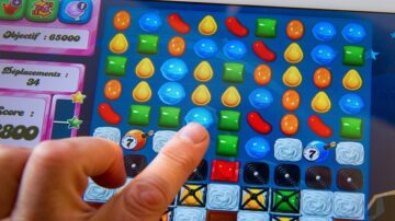 صورة تظهر شخصًا يستخدم إصبعه للعب لعبة كاجوال على جهاز لوحي. الشاشة تعرض شبكة من الأشكال الملونة، بما في ذلك الحلوى والزجاجات والمكعبات. تُظهر اللعبة أهدافًا مثل النقاط والمستويات المُنجزة.