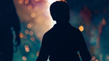 طفل silhouetted أمام عرض للألعاب النارية، مع أضواء ملونة تتلألأ في الخلفية، مشهد يعبر عن الفرح والاحتفال.