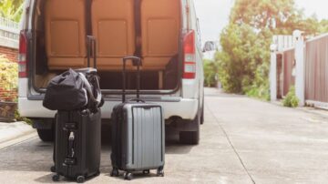 حقائب سفر موضوعة بجانب van مفتوح في شارع هادئ. تظهر حقيبة كبيرة وسلسلة حقائب صغيرة، مع مقبض قابل للسحب. تضفي الإضاءة الطبيعية شعورًا بالراحة على المشهد.