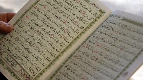 صفحتان من كتاب باللغة العربية وحواف مزخرفة، يمسك بهما شخص.