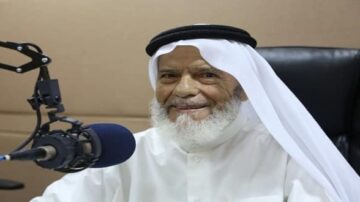 رجل مسن يرتدي الثوب السعودي والشماغ، يجلس أمام ميكروفون في استوديو إذاعي، مبتسمًا ويبدو سعيدًا.