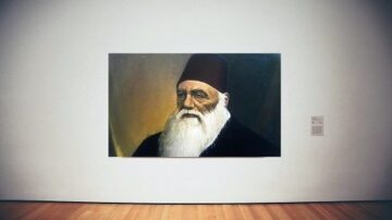 صورة لعمل فني يظهر رجل مسن ذو لحية بيضاء مرتديًا عمامة حمراء، مع خلفية داكنة. اللوحة معروضة في متحف على جدار أبيض، والأرضية خشبية.