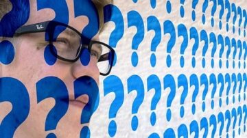 شخص يرتدي نظارات يظهر مع خلفية مكونة من علامات استفهام زرقاء، تعبر عن التساؤل والفضول.