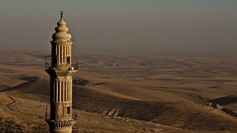 مئذنة حجرية في منظر صحراوي واسع تحت سماء مغبرة.