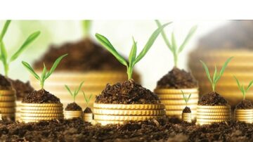 نبتات خضراء صغيرة تنمو من أكوام من العملات الذهبية على تربة غنية، تعبر عن فكرة النمو المالي والاستثمار المستدام.