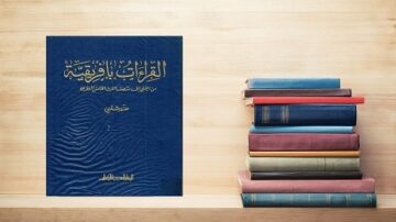 كتاب أزرق عن القراءات القرآنية بجانب كومة كتب ملونة على رف خشبي.
