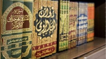 كتب إسلامية ملونة ومرتبة على رف خشبي، تحتوي على نصوص عربية تقليدية، تعكس التراث الثقافي والديني.