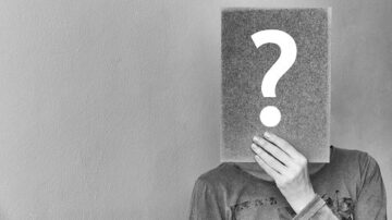 شخص يحمل ورقة بها علامة استفهام، يظهر من الصدر إلى الأعلى، مع خلفية بسيطة. تعبيره يوحي بالاستفسار أو الغموض.