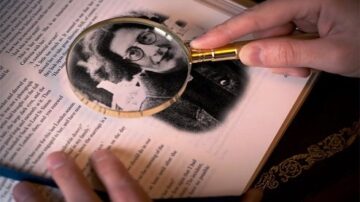 صورة تظهر يدين تحملان عدسة مكبرة فوق صفحة كتاب تحتوي على صورة تاريخية لرجل يرتدي نظارات. تركز العدسة على تفاصيل الصورة، مما يبرز معالم الوجه والملابس.