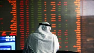 رجل يرتدي الزي العربي التقليدي يتأمل شاشة تعرض أسعار الأسهم وأرقام السوق المالية بألوان متغيرة في بيئة تداول.