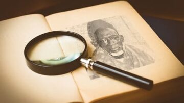 صورة تظهر عدسة مكبرة موضوعة على صفحة كتاب قديم تحتوي على صورة لرجل مسن. تعكس الصورة التراث الثقافي والتاريخي، مما يعزز أهمية الوثائق القديمة في البحث والدراسة.