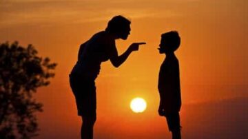 امرأة توبخ طفلًا في ظل غروب الشمس، حيث يظهر silhouetted الشكلين أمام ألوان السماء الدافئة. تعكس الصورة لحظة تعليمية أو تأديبية في علاقات الأسرة.