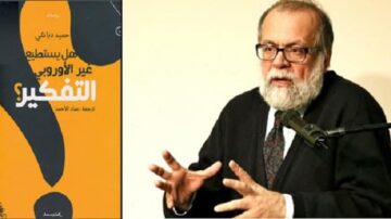 رجل مسن ذو لحية وشعر رمادي يتحدث في حدث، مع التركيز على تعبير وجهه. خلفه كتاب بعنوان "هل يستطيع غير الأوروبي التفكير؟" باللون الأسود والبرتقالي. الصورة تعكس مناقشة فكرية حول مواضيع فلسفية وثقافية.