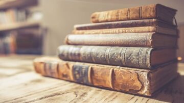 مجموعة من الكتب القديمة المصفوفة بشكل جميل على طاولة خشبية، تظهر تفاصيل الغلاف والتآكل مما يبرز تاريخها.