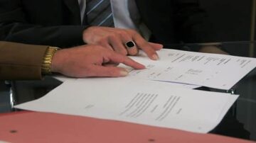 أيدٍ تشير إلى مستندات قانونية موضوعة على طاولة زجاجية، مع التركيز على تفاصيل النصوص والأرقام.