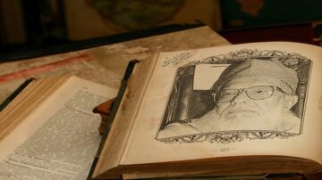 صورة لكتاب قديم مفتوح يظهر صفحة تحتوي على رسم تخطيطي لرجل مسن ذو لحية وشعر أبيض، يرتدي نظارات. الكتاب موضوع على طاولة بالقرب من كتب أخرى قديمة.