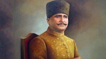 صورة لرجل يرتدي زيًا تقليديًا مزخرفًا ويجلس على كرسي. يحمل الرجل لحية وشوارب ويظهر تعبيره الجاد. الخلفية غامقة تضيف طابعًا تاريخيًا.