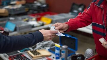 تبادل نقود بين شخصين في سوق للأدوات، مع تفاصيل عن الأدوات المعروضة في الخلفية.