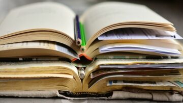 كتاب مفتوح مع صفحات متقلبة، يحتوي على دفتر ملاحظات وأقلام ملونة، مع أوراق إضافية ومواد مكتبية.