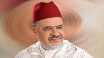 صورة لرجل يرتدي لباسًا تقليديًا مغربيًا مع عمامة حمراء، يظهر بتعبير هادئ. الخلفية تحتوي على دوائر ملونة تعكس طابعًا فنيًا.