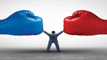 رجل يرتدي بدلة يقف بين قفازين ملاكمة زرقاء وحمراء ضخمة، مما يعكس صراعًا أو تنافسًا. تعبير عن التحدي والضغط في بيئة العمل أو الحياة.