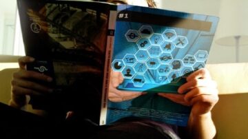 شخص جالس على أريكة يقرأ مجلة تحتوي على تصميم عصري، مع صور رموز تقنية وأزرار. المجلة مفتوحة في يد الشخص، مما يبرز محتوى بصري جذاب.