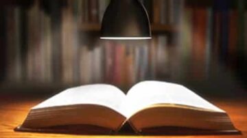 كتاب مفتوح تحت ضوء مصباح، مع خلفية مكتبة ضبابية، يرمز إلى القراءة والمعرفة.