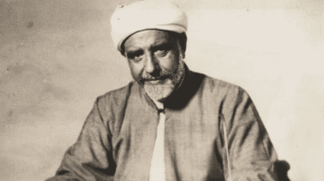 صورة تاريخية لرجل مسن يرتدي عمامة بيضاء وثوب تقليدي، يظهر بابتسامة خفيفة. تعكس الصورة تراث وثقافة المنطقة، مع تفاصيل واضحة تعبر عن الزمن القديم.