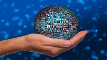 كرة أرضية تحتوي على صور متعددة لأشخاص، تُعقد في يد بشرية، مع خلفية زرقاء مضيئة. تعبر الصورة عن الاتصال والتواصل العالمي.