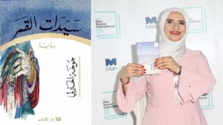 امرأة ترتدي حجاباً تحمل كتاب "سيدات القمر" بجانب لوحة جائزة "Man Booker International".