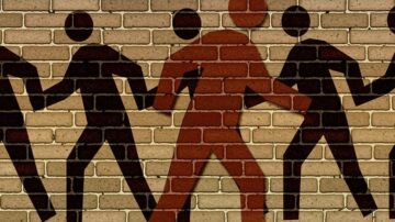 صورة لجدار مكون من طوب بأشكال بشرية. يظهر شخص واحد ملون بلون مميز يسير بين أشكال بشرية أخرى باللون الأسود، مما يبرز فكرة التميز والفردية في المجتمع.