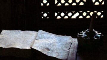 كتاب قديم مفتوح بجوار أداة كتابة تقليدية، مع نافذة منقوشة في الخلفية، تضيء المكان برفق.