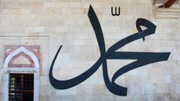 خط عربي كبير يحمل اسم محمد مكتوب بأناقة على جدار مبنى تاريخي، مع خلفية من الحجر. يبرز التصميم الفني للخط في مكانه، مما يعكس الثقافة الإسلامية.